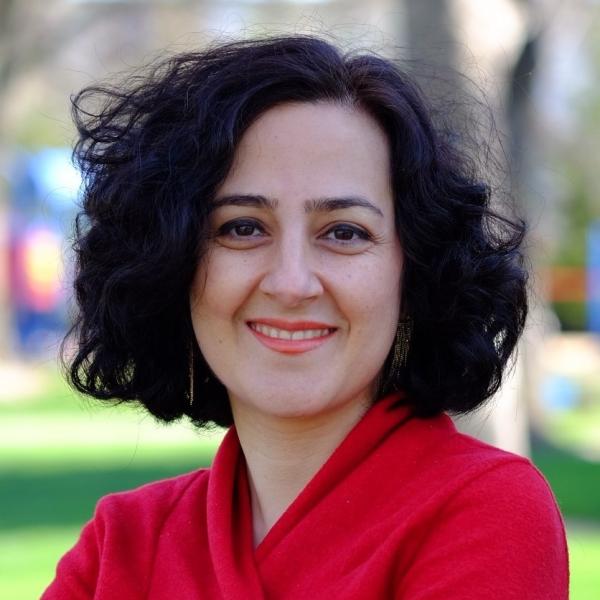 Image of a woman with shoulder-length black curly hair wearing a red shirt, with green grass in the background.